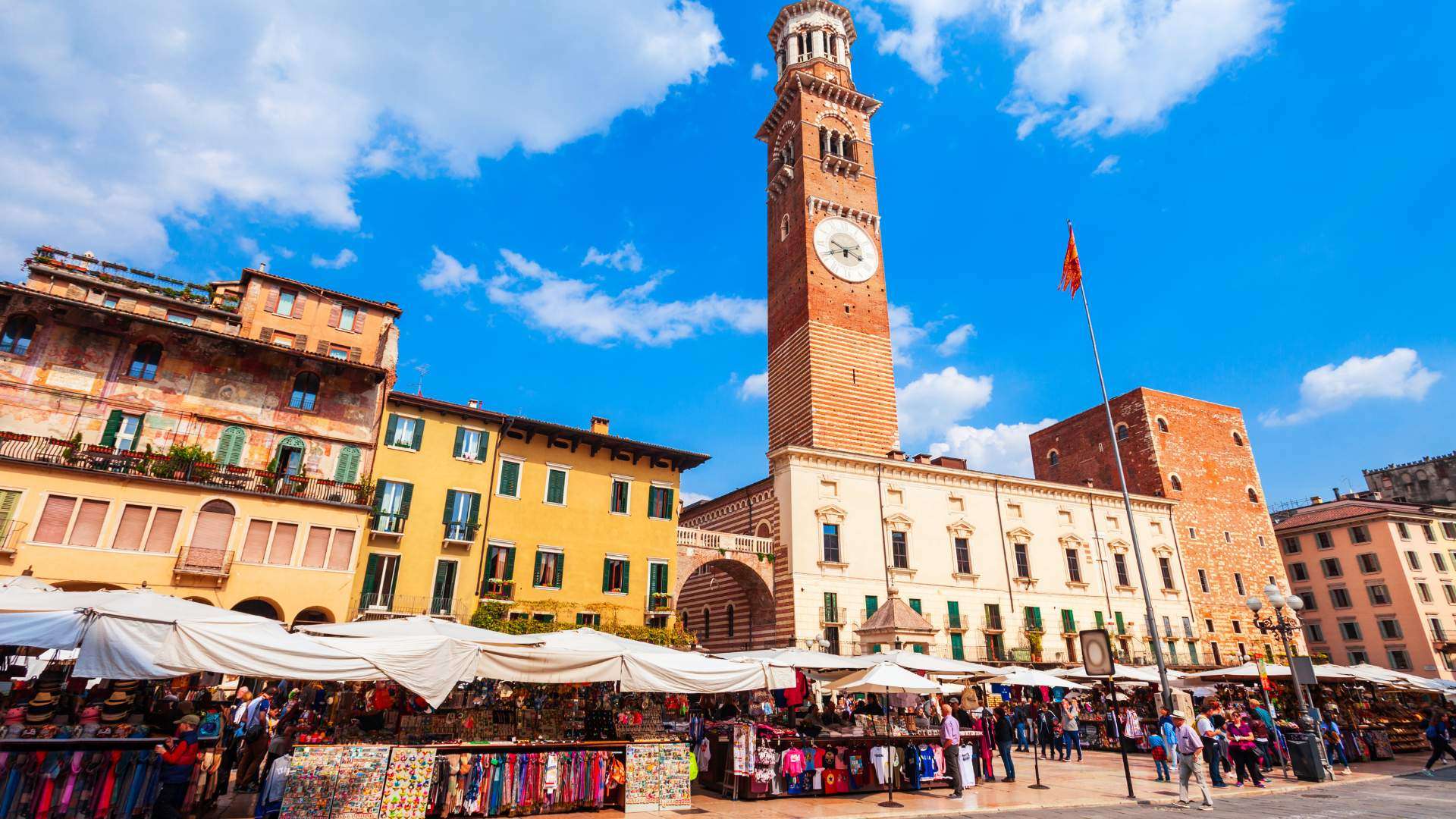 Torre dei Lamberti, Piazza delle Erbe, Verona, Venetien, Italien (Credits CanvaPro) Torre dei Lamberti über der sonnigen Piazza delle Erbe mit Marktständen in Verona