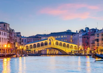 Beleuchtete Rialtobrücke über dem Canal Grande in der Abenddämmerung in Venedig