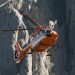 Orangefarbener Bergrettungshubschrauber im Flug vor den schroffen Felswänden der Dolomiten (Symbolbild)