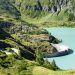 Stausee in den Alpen, umgeben von bewaldeten Berghängen (Symbolbild)