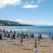 Sonniger Strand auf Sizilien mit Reihen von Sonnenschirmen und Badegaesten am Meer