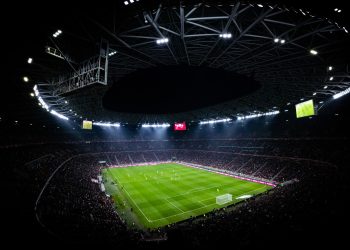 Nächtliches Fußballstadion im Flutlicht mit vollen Rängen vor Anstoß eines Topspiels