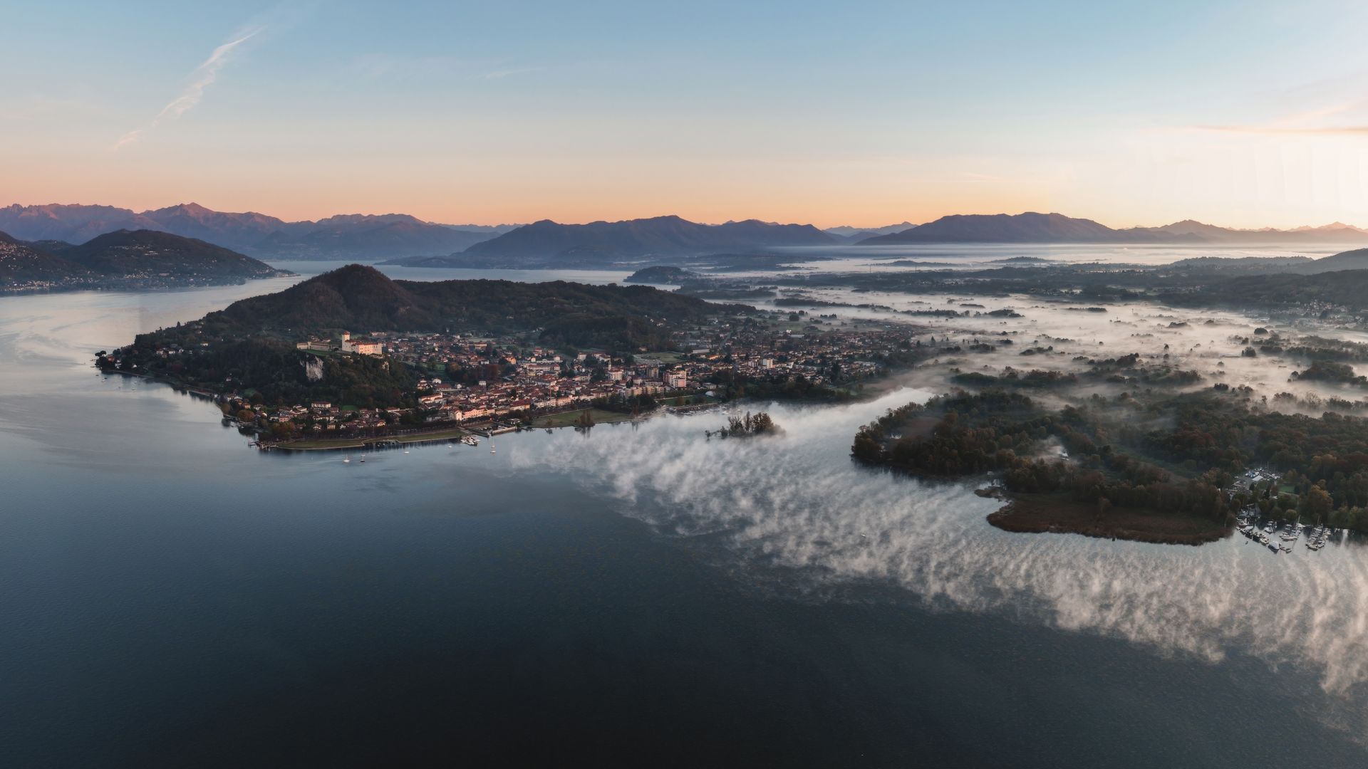 Morgennebel über dem Lago Maggiore mit bewaldeten Hügeln bei Sonnenaufgang