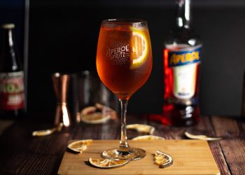Leuchtend orangefarbener Aperol Spritz mit Orangenscheibe, im Hintergrund eine Aperol-Flasche
