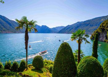 Der Comer See mit bewaldeten Steilufern und den Bergen der Lombardei im Hintergrund