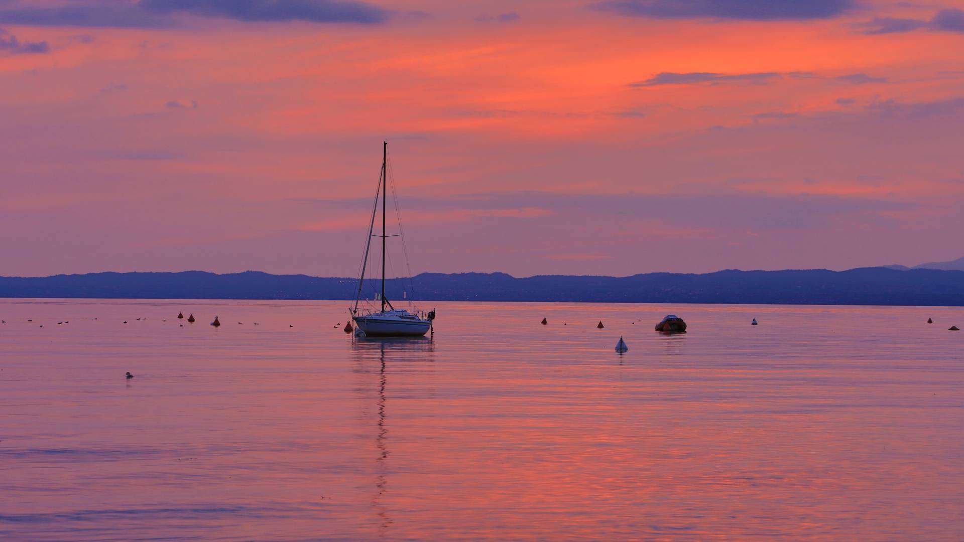 Rosa gefärbter Abendhimmel über dem Gardasee mit einem Segelmast im Gegenlicht