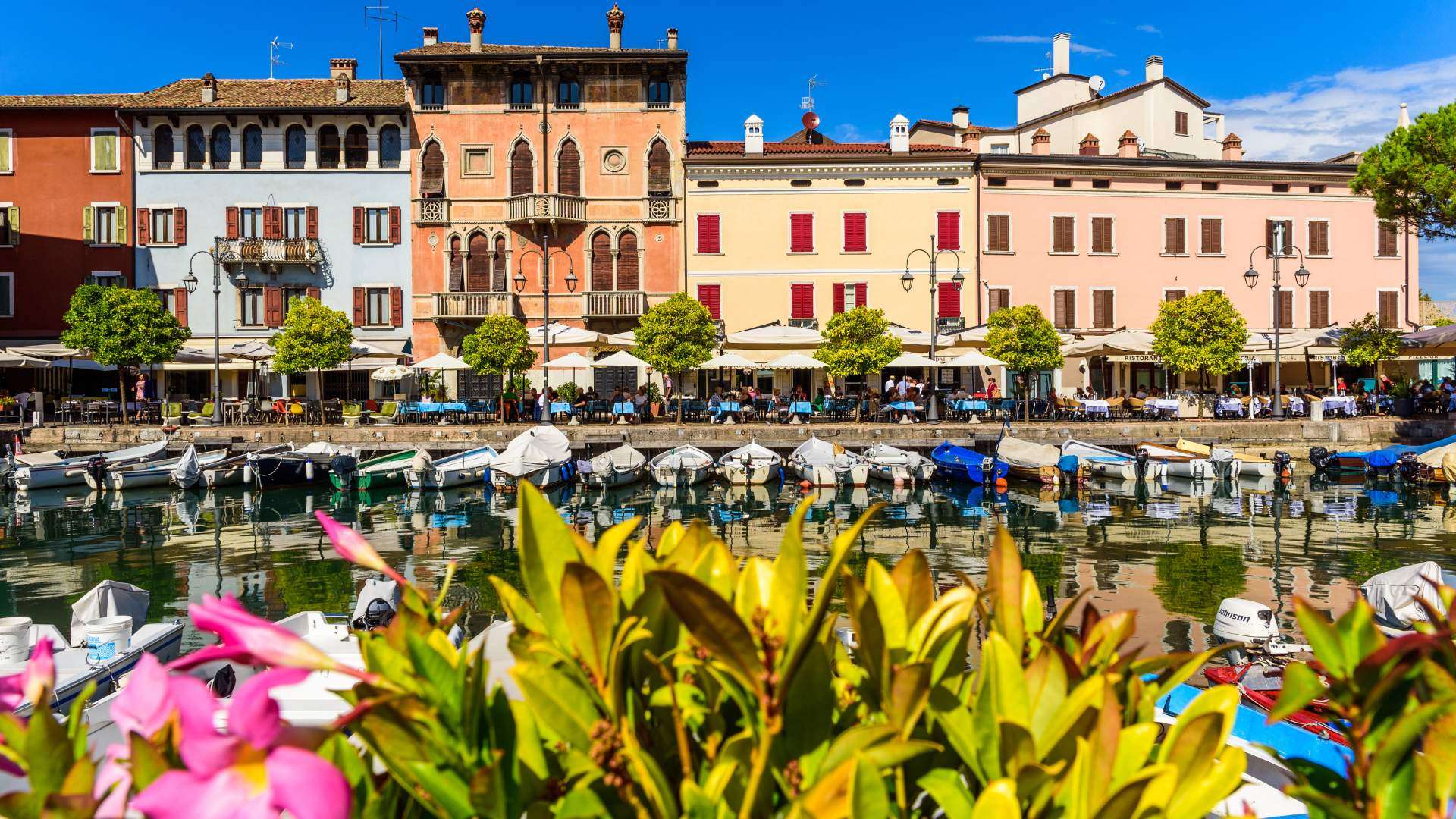 Pastellfarbene Häuserzeile am Hafen von Desenzano del Garda mit Blumen im Vordergrund