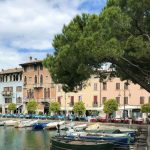 Boote im Porto Vecchio von Desenzano del Garda vor pastellfarbenen Häusern und Pinien