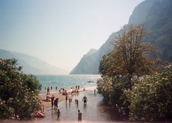 Badegäste schwimmen und sonnen sich an einem Ufer des Gardasees vor der Bergkulisse
