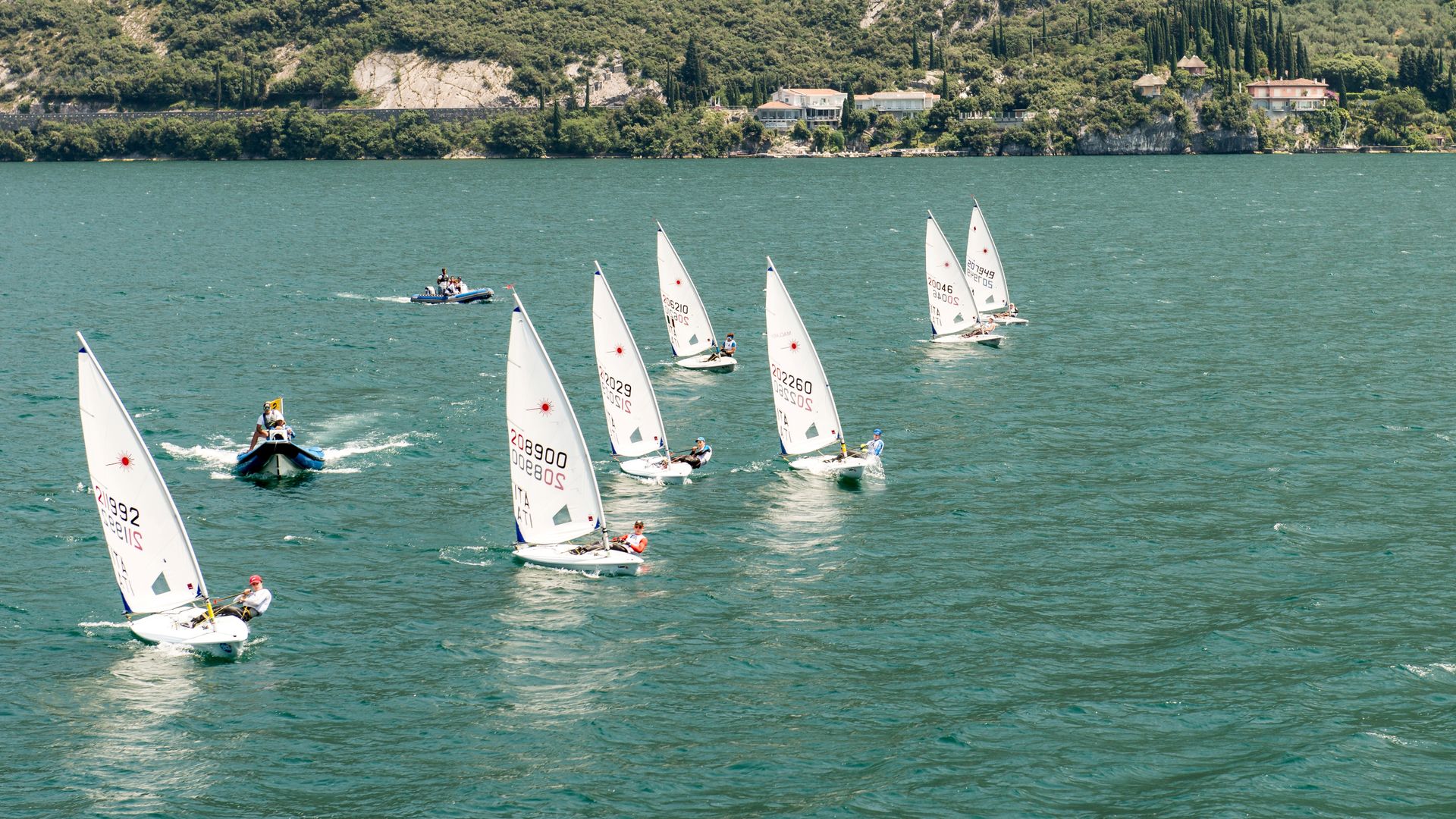 Segelboote auf dem Gardasee aus der Vogelperspektive, dahinter das bewaldete Ufer