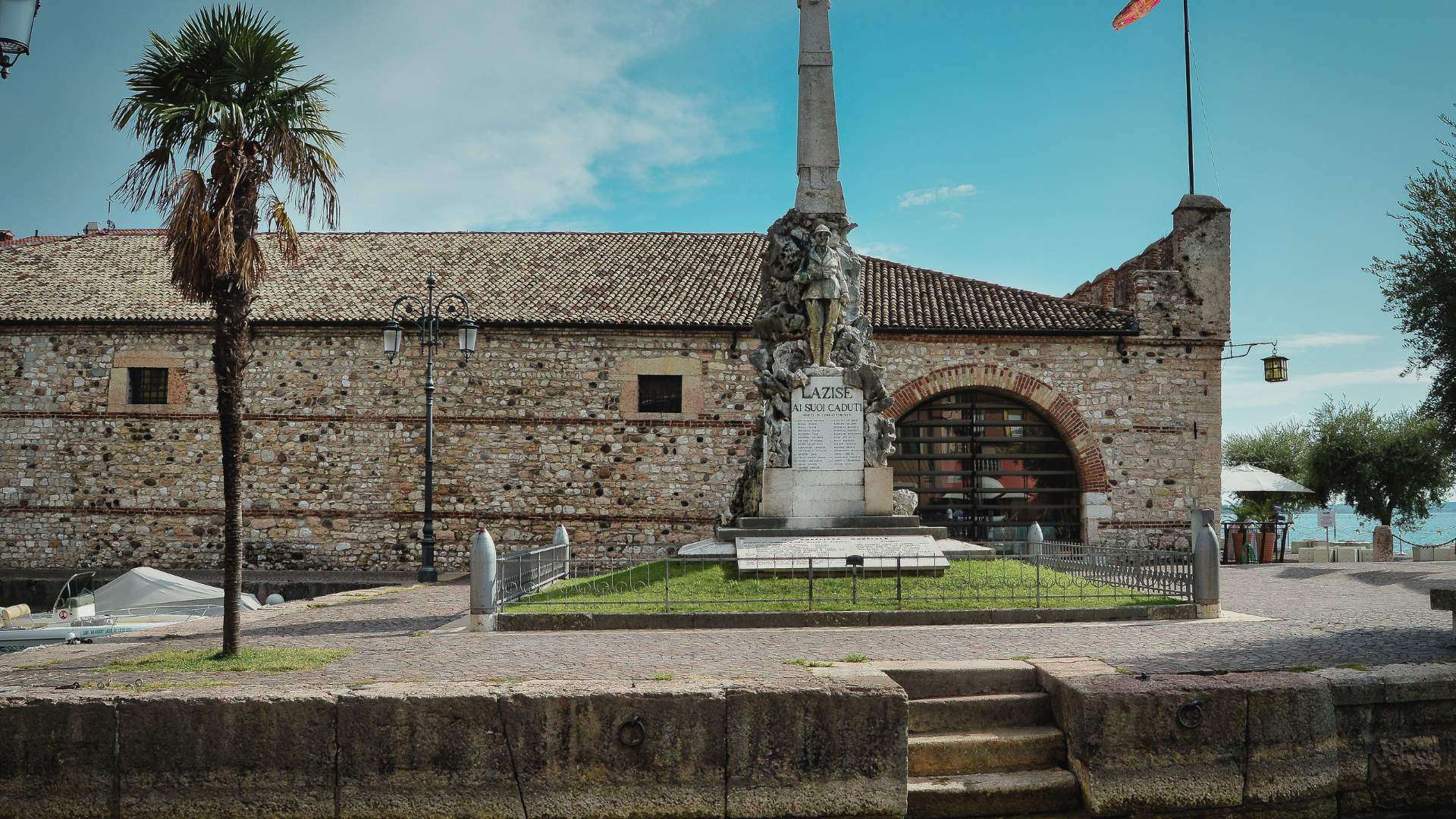 Denkmal auf der Piazza Vittorio Emanuele II in Lazise mit Arkaden und Palme