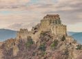 Die Abtei Sacra di San Michele auf ihrem Felsgrat im warmen Abendlicht, dahinter die Berge des Val di Susa