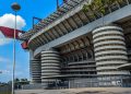 Das Stadion San Siro in Mailand von außen mit den runden Rampentürmen und den roten Dachträgern unter blauem Himmel