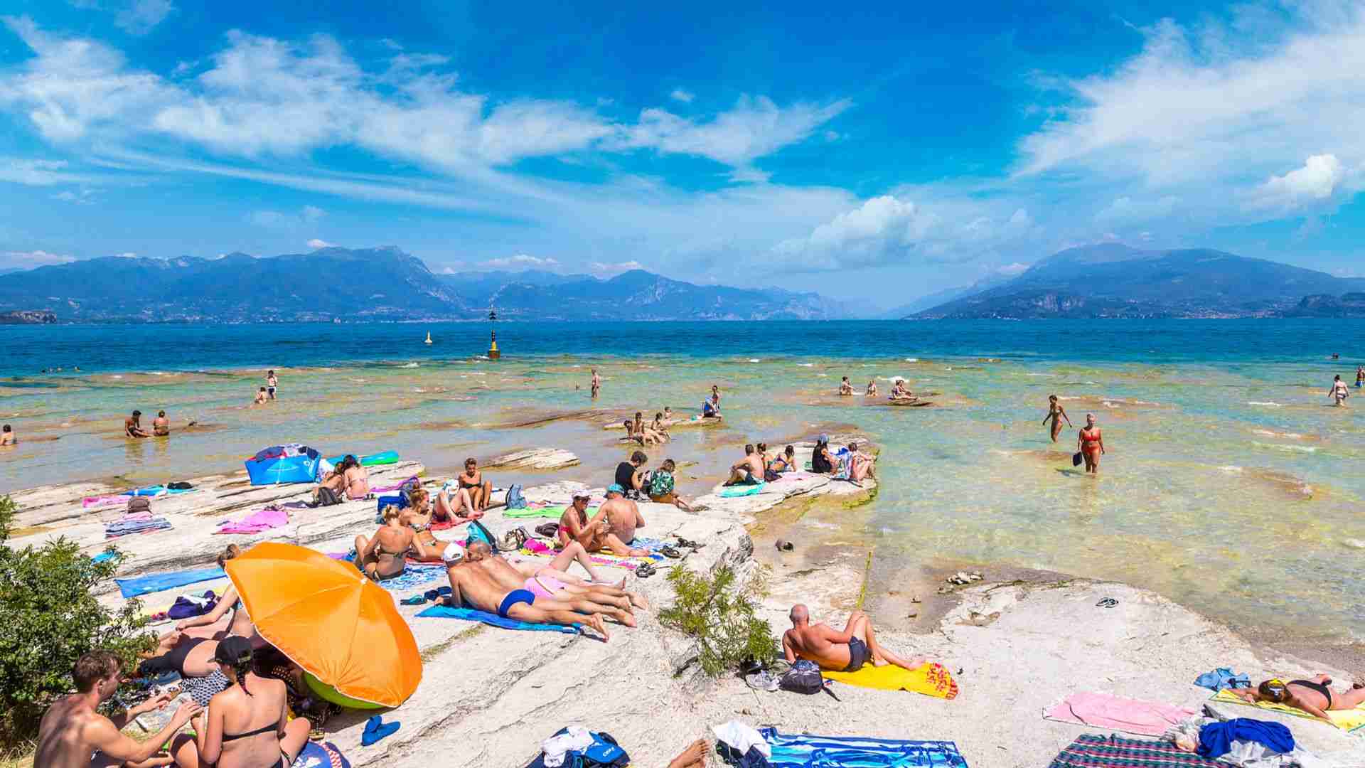 Badegäste auf dem flachen weißen Fels der Spiaggia Giamaica in Sirmione