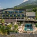 Luftaufnahme des Hotels Hilburger in Schenna mit begrünten Balkonen, Terrasse und Pool vor bewirtschafteten Hängen