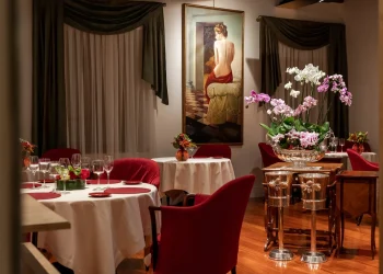 Gastraum mit gedeckten Tischen, roten Sesseln, Orchideen und einem großen Gemälde an der Rückwand