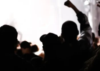 Silhouetten mehrerer Menschen vor hellem Rauch, eine Person hebt die geballte Faust – Symbolbild