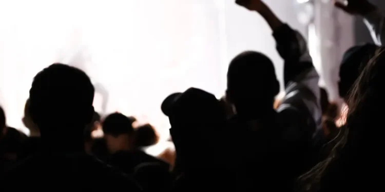 Silhouetten mehrerer Menschen vor hellem Rauch, eine Person hebt die geballte Faust – Symbolbild