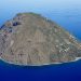 Die Insel Alicudi mit steilen Hängen und Küstensiedlung im blauen Tyrrhenischen Meer, von Süden aus der Luft gesehen