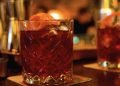 Zwei Kristallgläser mit rotem Aperitif, Eis und Orangenzeste auf einem Bartresen im warmen Licht