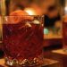 Zwei Kristallgläser mit rotem Aperitif, Eis und Orangenzeste auf einem Bartresen im warmen Licht