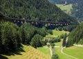 Lange Autobahnbrücke auf hohen Betonpfeilern über einem bewaldeten Alpental mit Wiesen im Talgrund