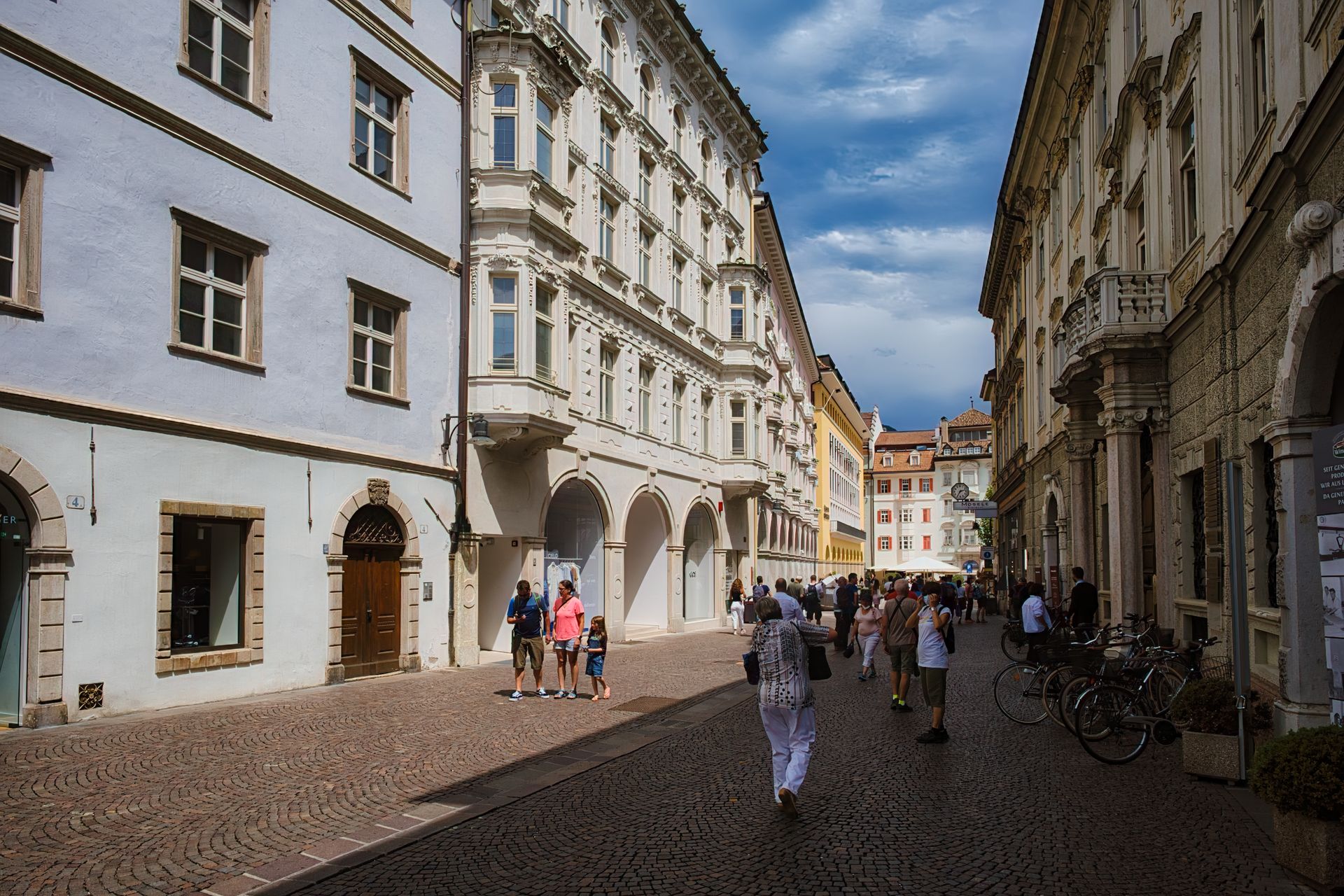Altstadtgasse in Bozen Gepflasterte Gasse zwischen hellen Altstadthäusern in Bozen, Passanten und abgestellte Fahrräder