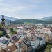 Blick über die Dächer der Brunecker Altstadt mit Kirchturm, dahinter die bewaldeten Berge des Pustertals
