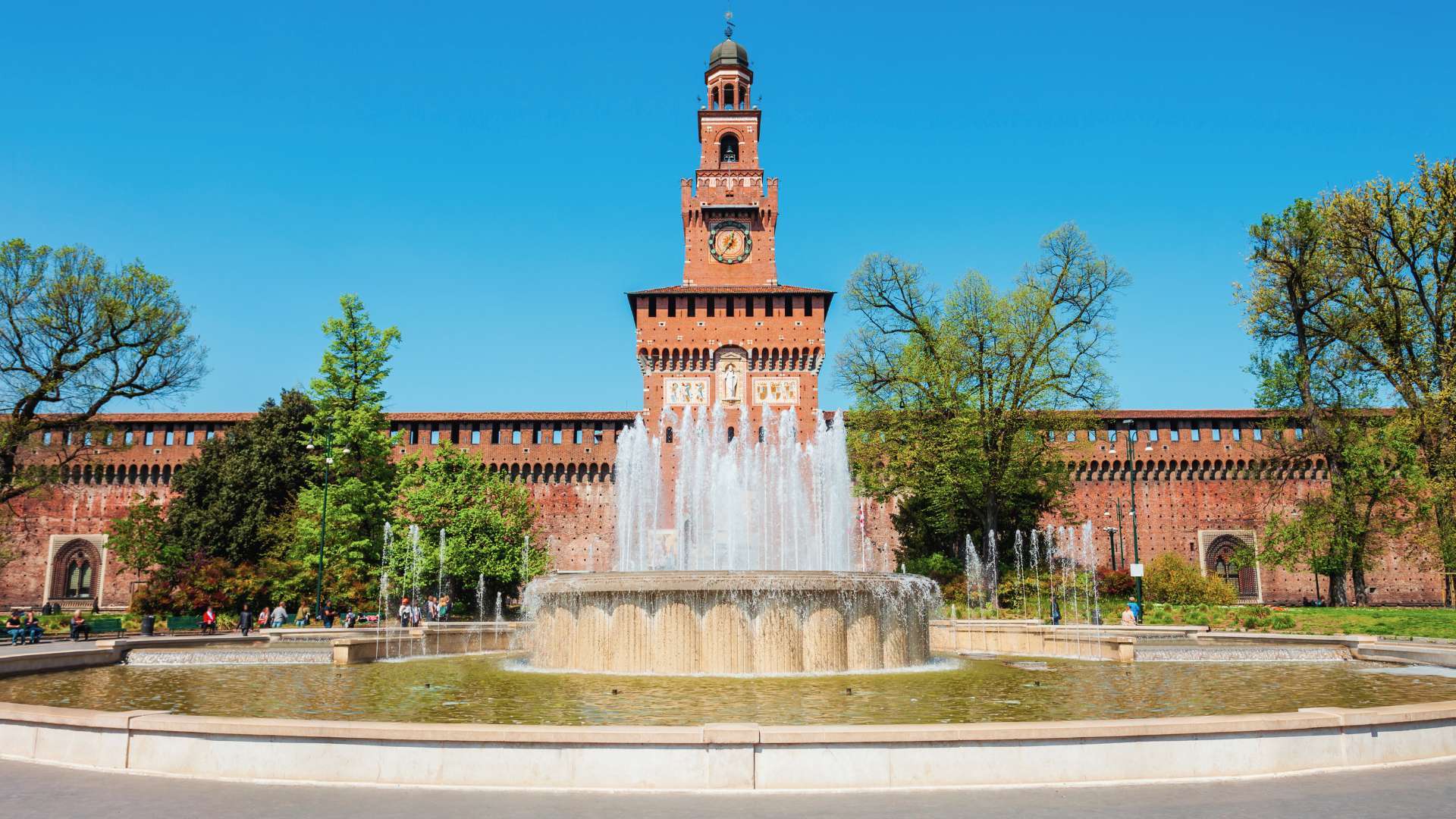 Der Torre del Filarete des Castello Sforzesco hinter dem Springbrunnen der Piazza Castello unter blauem Himmel