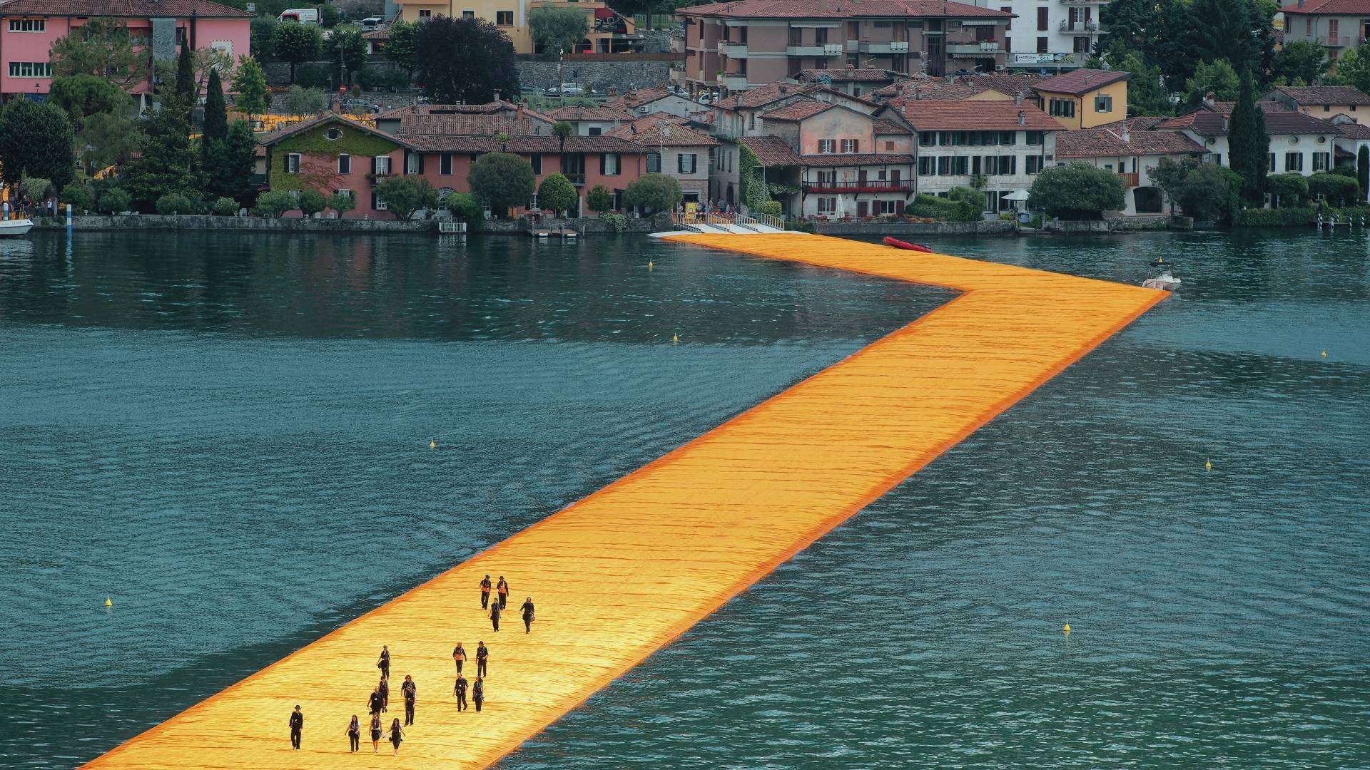 Floating Piers auf dem Iseosee 2016 Gelber schwimmender Steg der Floating Piers auf dem Iseosee mit Spaziergängern, dahinter Häuser am Ufer