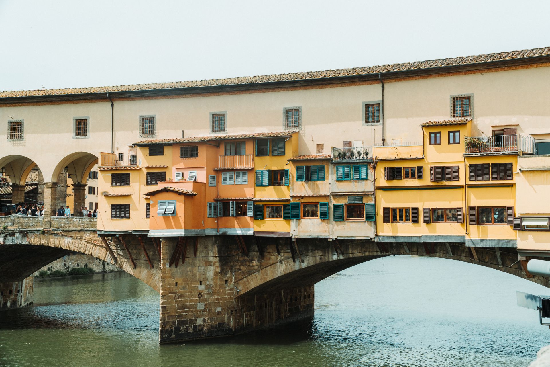 Die Ponte Vecchio in Florenz mit ihren bunten Ladenhäusern auf Steinbögen über dem grünen Wasser des Arno