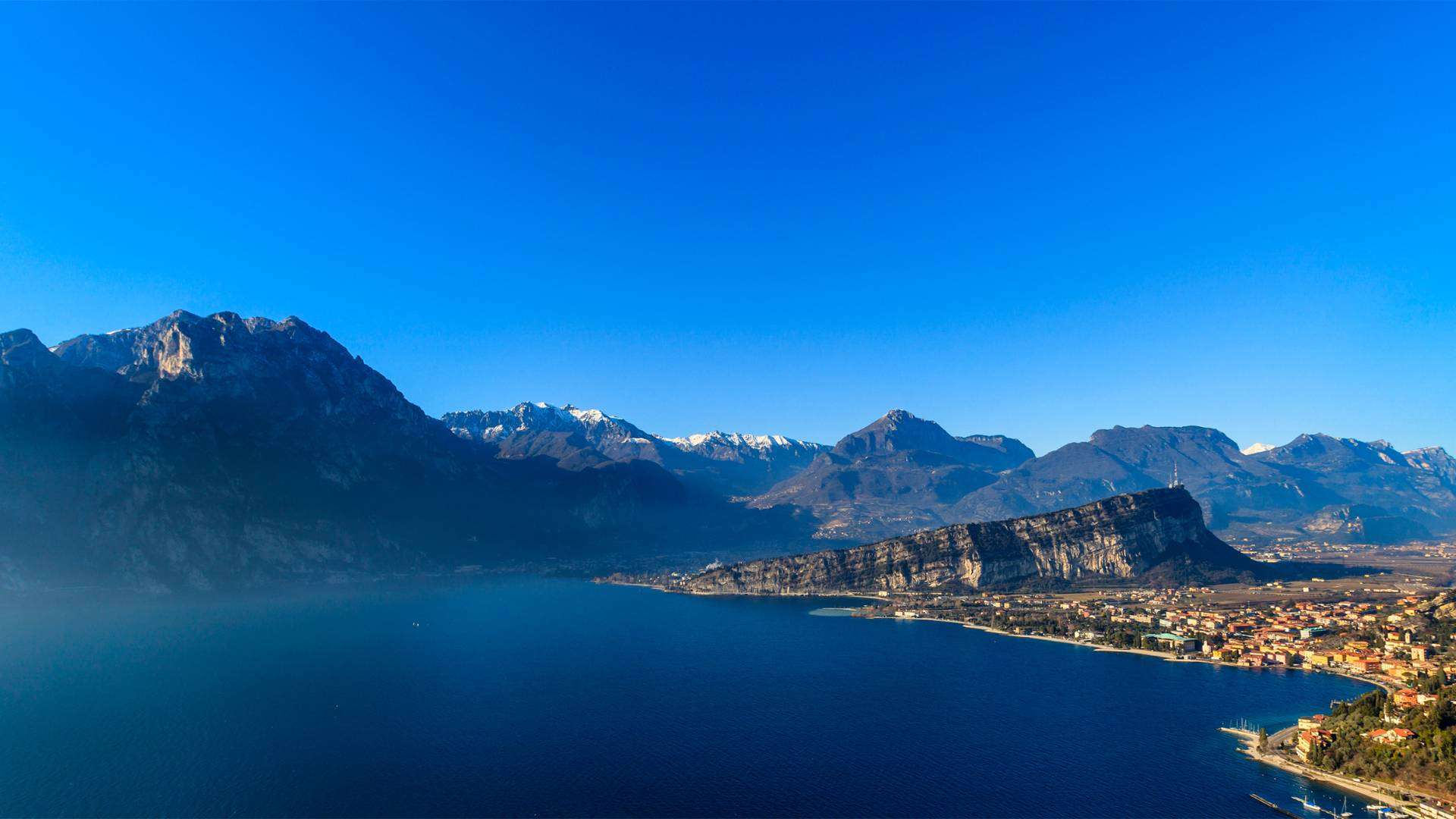 Weiter Blick über das tiefblaue Nordufer des Gardasees bei Torbole mit Bergketten im Hintergrund