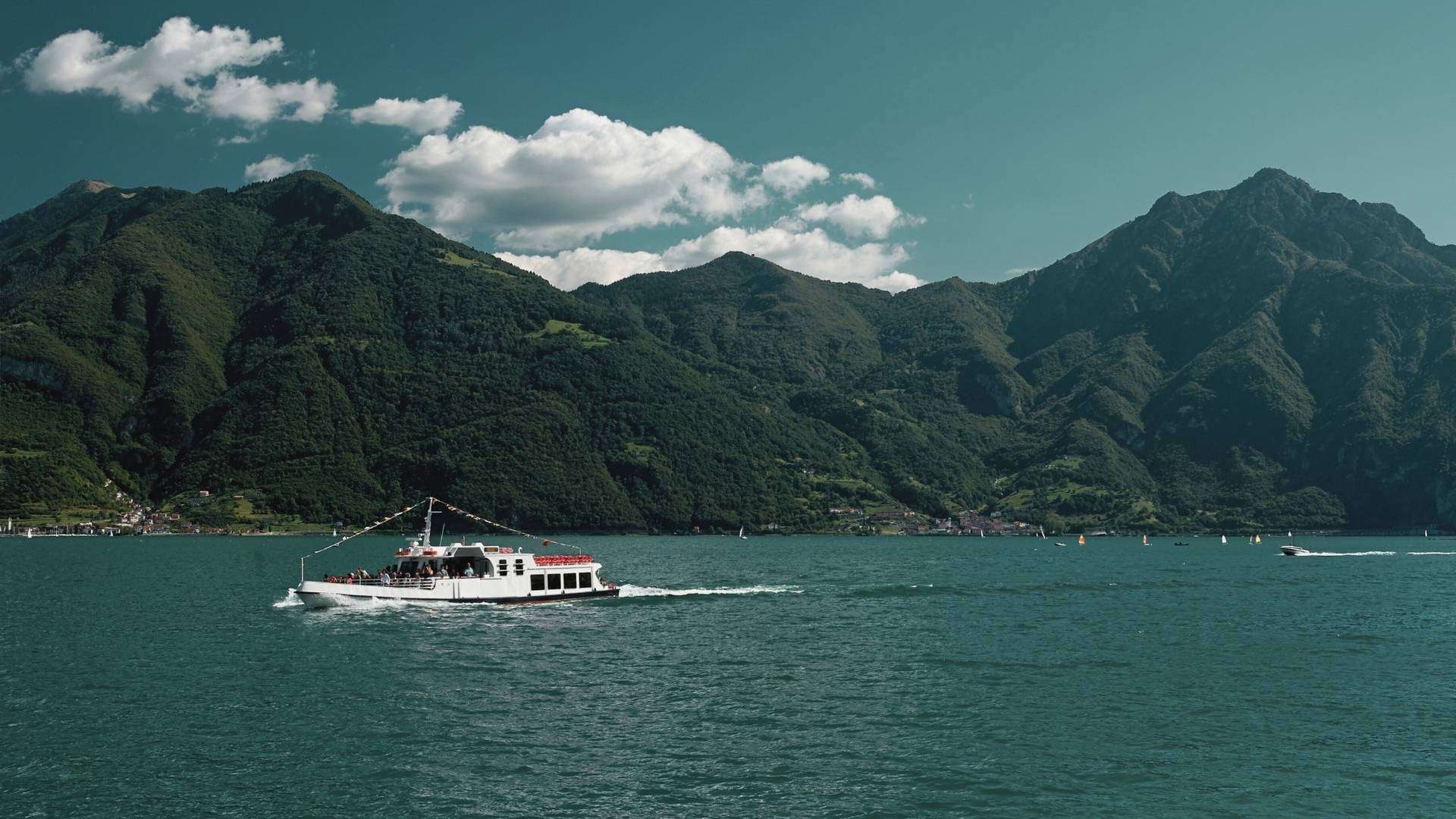 Weißes Ausflugsschiff auf dem Iseosee Weißes Schiff auf dem Iseosee vor grünen Bergen und Wolken
