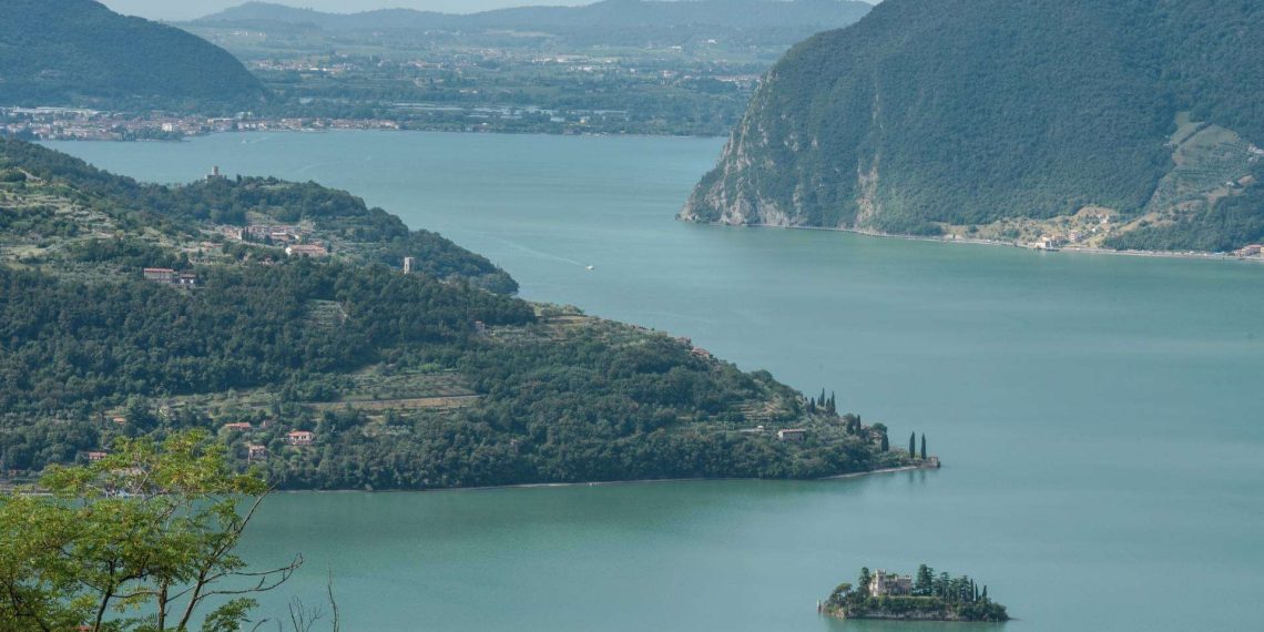 Blick über den Iseosee auf Monte Isola und eine kleine Insel mit Villa, dahinter Berge