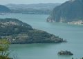 Blick über den Iseosee auf Monte Isola und eine kleine Insel mit Villa, dahinter Berge
