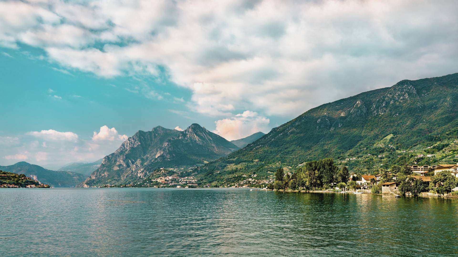 Wolken über dem Iseosee und den Bergen Iseosee mit grünen Bergen am Ufer unter großen Wolken
