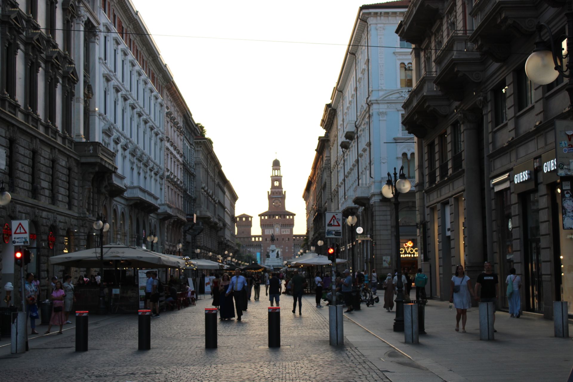 Belebte Fußgängerstraße in Mailand am Abend mit Cafétischen und dem Torre del Filarete am Ende der Straße