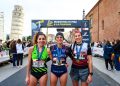 Drei Läuferinnen mit Medaillen vor dem Zielbogen der Maratona di Pisa, links im Hintergrund der Schiefe Turm