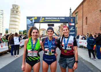 Drei Läuferinnen mit Medaillen vor dem Zielbogen der Maratona di Pisa, links im Hintergrund der Schiefe Turm