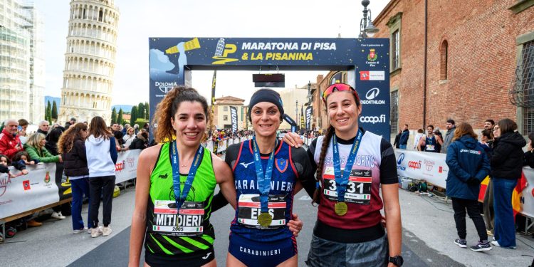 Drei Läuferinnen mit Medaillen vor dem Zielbogen der Maratona di Pisa, links im Hintergrund der Schiefe Turm