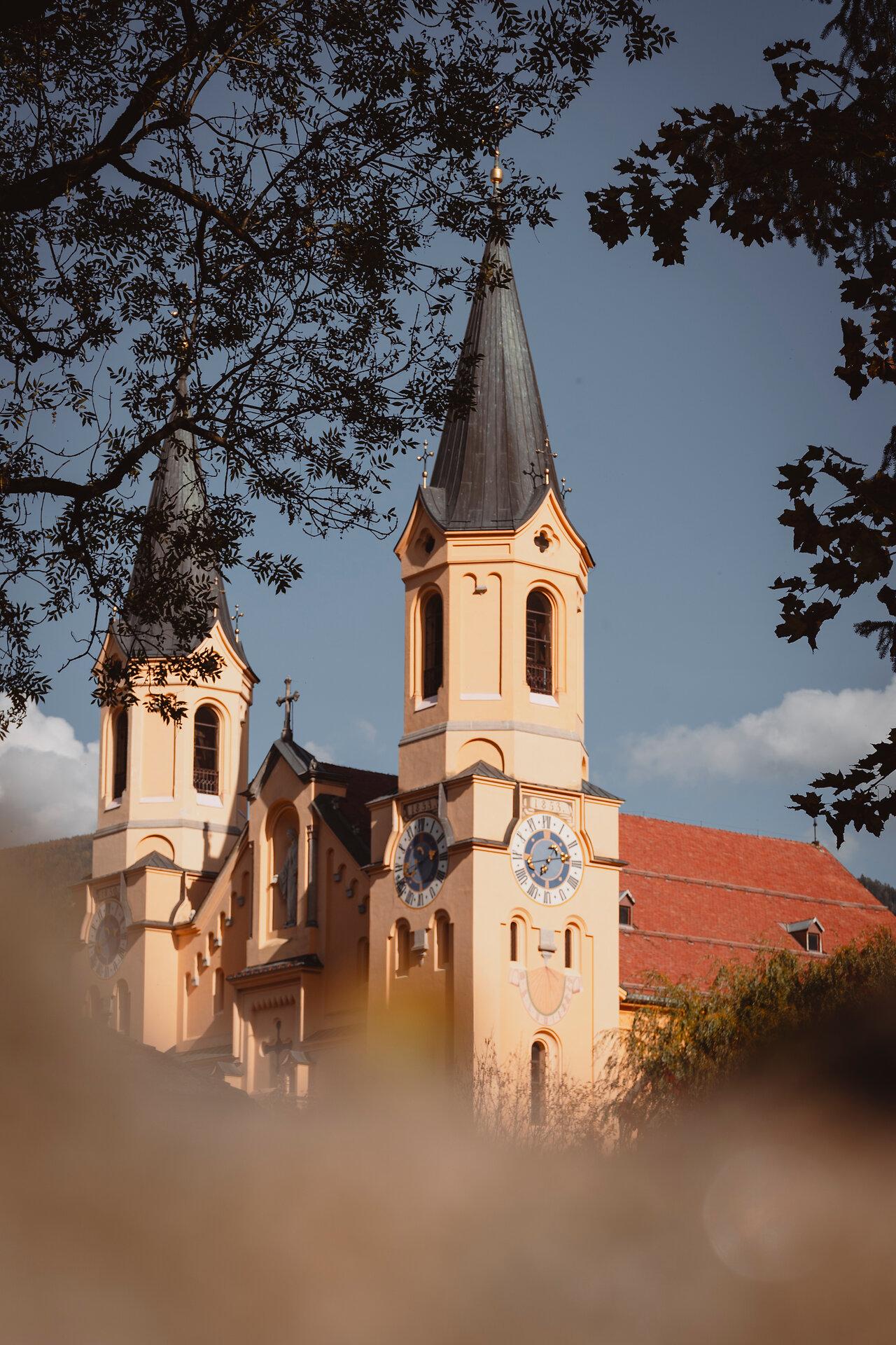 Die beiden Türme der Brunecker Pfarrkirche im warmen Licht, eingerahmt von Ästen