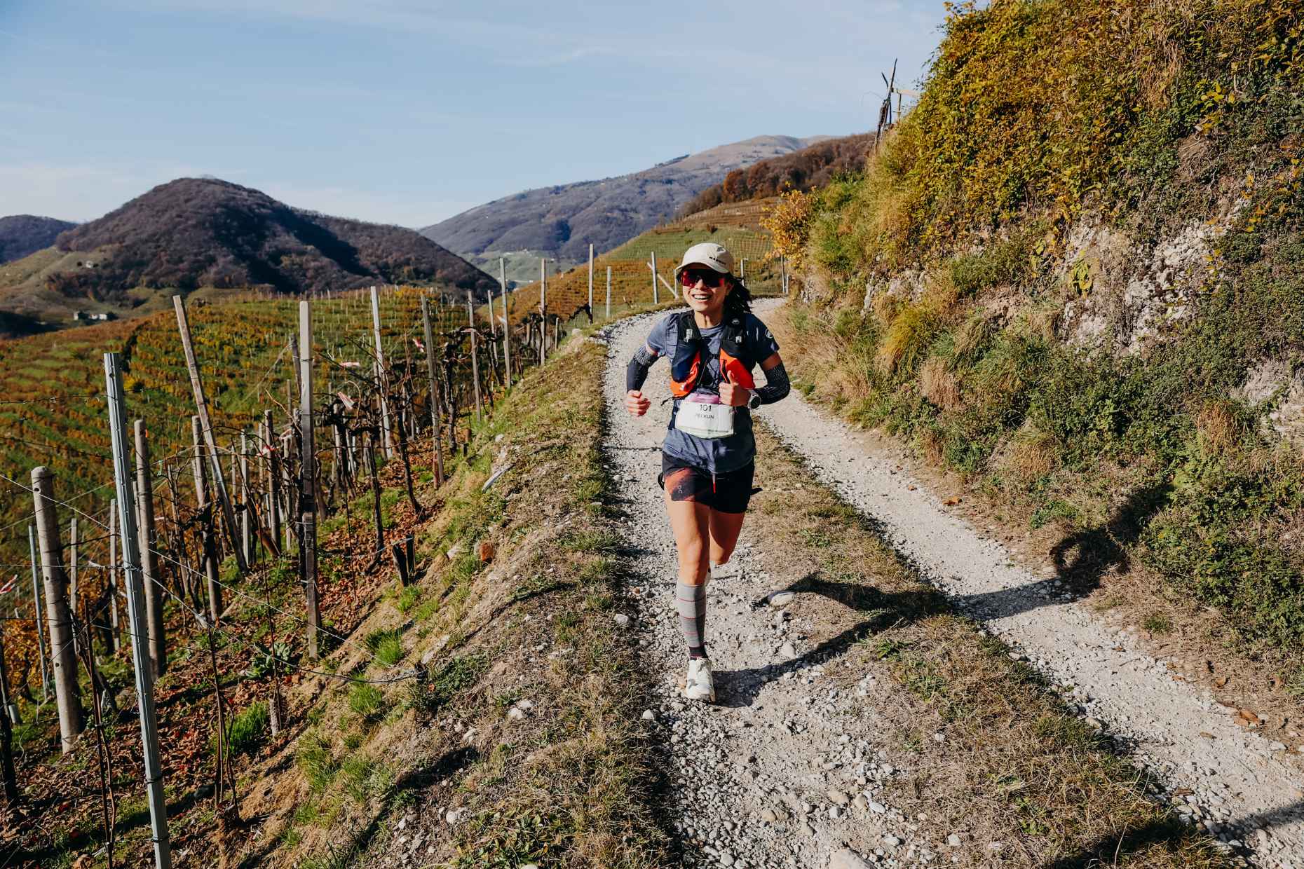 Prosecco-Hügel – Läuferin auf einem Schotterweg zwischen Reben Läuferin mit Laufweste auf einem Schotterweg am Hang zwischen Rebzeilen, im Hintergrund die Hügel um Valdobbiadene