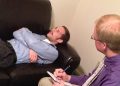 Ein Psychologe hört einem Mann auf einer Therapieliege zu, Symbolbild zur psychischen Gesundheitsversorgung