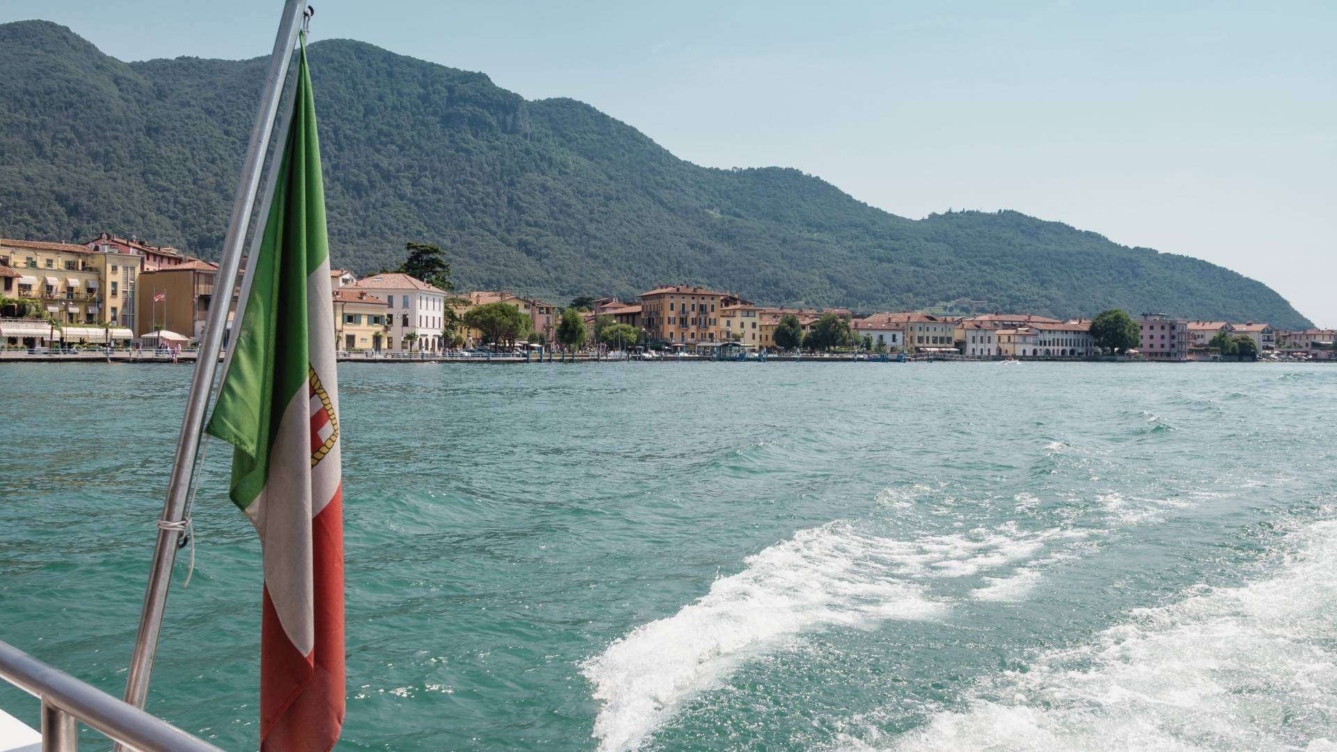 Mit dem Schiff über den Iseosee Heckwelle eines Schiffs mit italienischer Flagge auf dem Iseosee, im Hintergrund ein Uferort