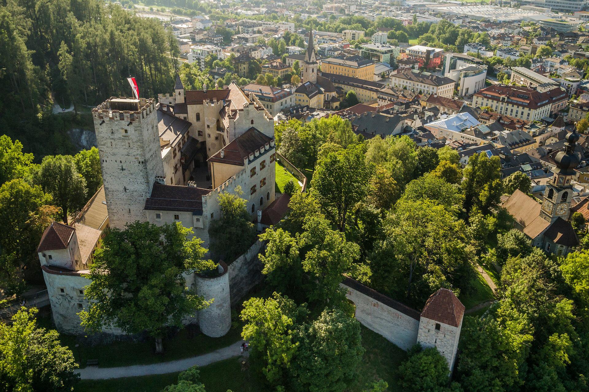 Luftbild von Schloss Bruneck mit seinem Turm, darunter die Dächer der Altstadt im Sommer