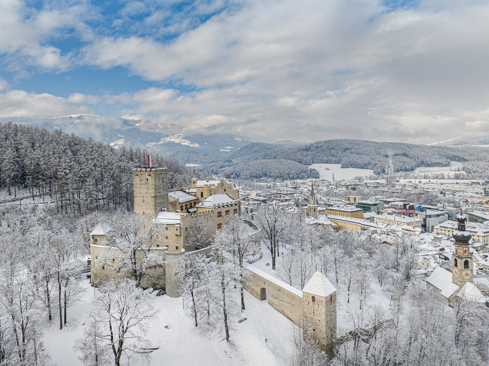 Schloss Bruneck und die verschneiten Bäume am Schlossberg, dahinter die Stadt im Winter