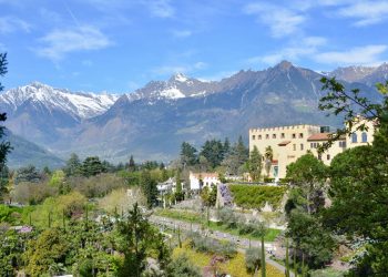 Schloss Trauttmansdorff mit seinen Gärten über Meran, dahinter schneebedeckte Gipfel unter blauem Himmel