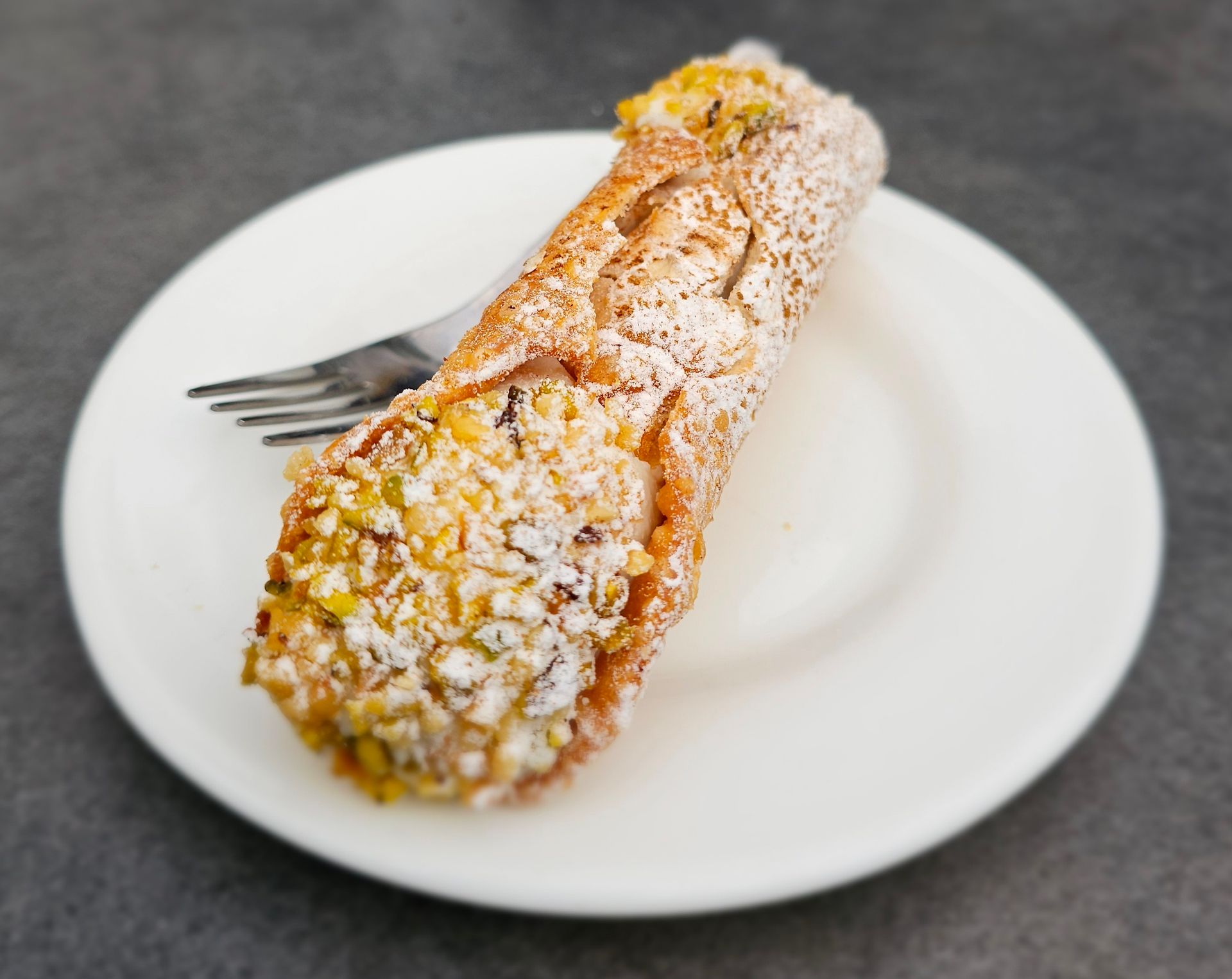 Sizilianisches Gebäck mit Ricotta Mit Ricotta gefülltes sizilianisches Gebäck mit Pistazien und Puderzucker auf einem Teller