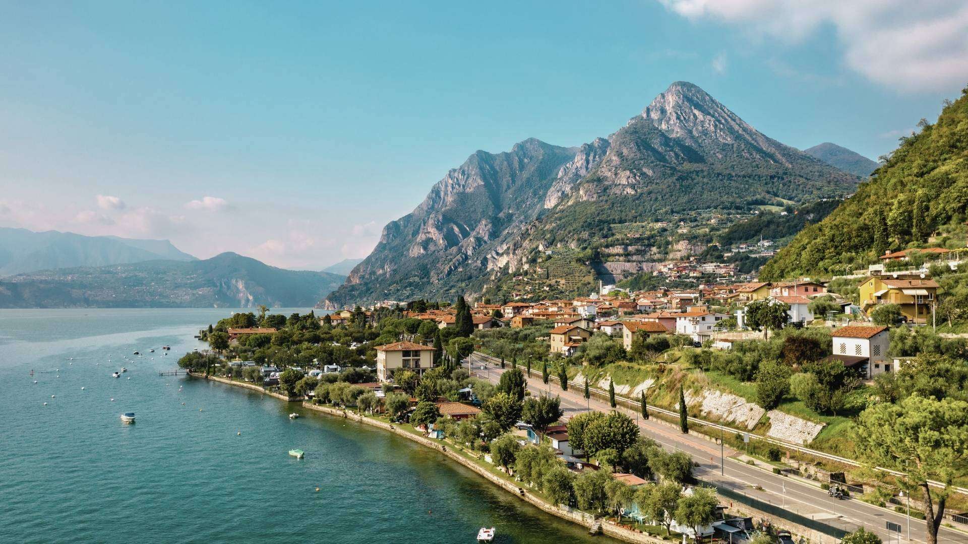 Uferort unter steilen Felsgipfeln am Iseosee Uferort am Iseosee mit Uferstraße, darüber ein steiler Felsgipfel